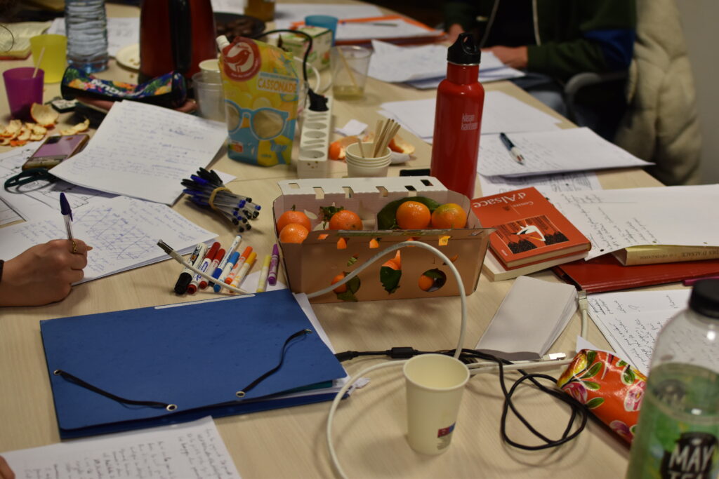 Table de l'atelier d'écriture recouverte de papiers, stylos, livres et collations.